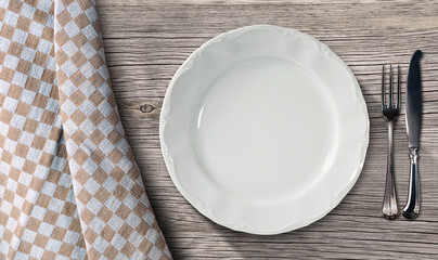 Plate and Cutlery on a Table with Tablecloth / Empty white plate on a table in pine wood with...