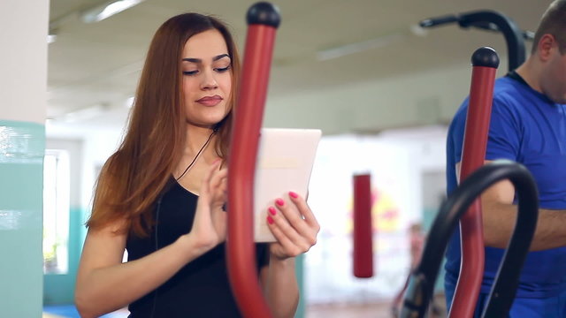 girl with  tablet sports man trainer ellipsoid on involved simulator 