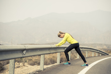 sport woman stretching leg muscle after running workout on asphalt road with dry desert landscape in hard fitness training session