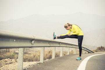 sport woman stretching leg muscle after running workout on asphalt road with dry desert landscape...
