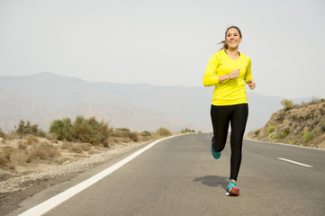 young attractive sport woman running on asphalt road with desert mountain landscape background