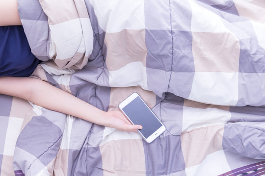 Woman sleeping and holding a mobile phone in the bed
