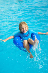 Fototapeta na wymiar Happy little boy with blue life ring has fun in the swimming pool
