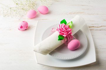 Pink Easter table place setting with plate, napkin and Pink Decorated Easter eggs on white wooden background, top view