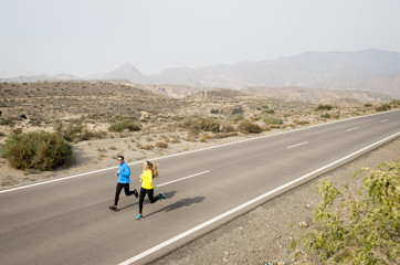 attractive sport couple man and woman running together on desert asphalt road mountain landscape