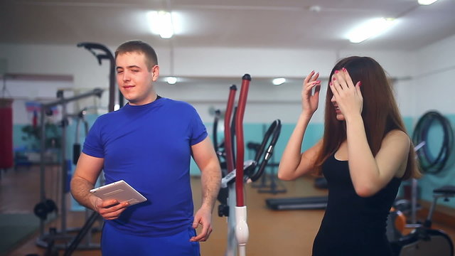 man with  a tablet in the gym, she straightens her bra