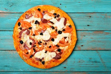 Rustic pizza with salami and olives on turquoise table