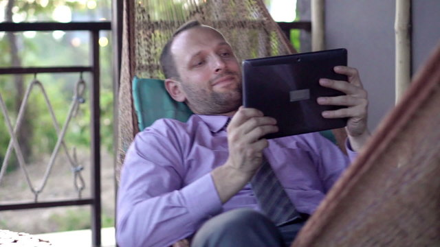 Businessman with tablet computer lying on hammock on the terrace
