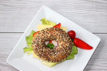 Vollkornbagel mit Käse, grünem Salat, Cherrytomate, Radieschen, Petersilie und Minipaprika auf modernem rechteckigem Teller angerichtet