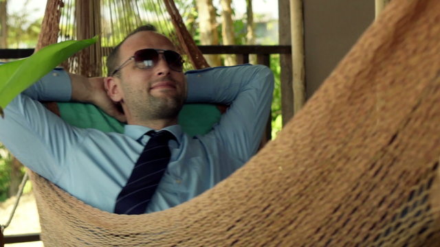 Happy businessman relaxing on hammock, at terrace
