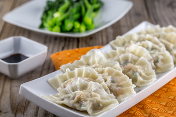 Chinese boiled pork and shrimp dumplings with soy sauce and green vegetables.