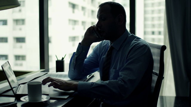 Angry businessman talking on cellphone by desk at office
