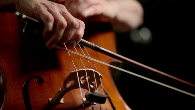 Hands and bow of a cellist playing a cello in real time.