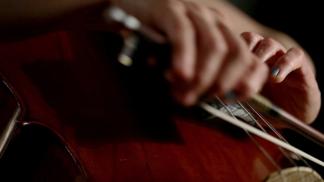 Close macro shot focusing on a cellist left hand technique as she performs high on her instruments fingerboard.