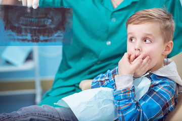 Dental inspection is being given to little boy surrounded by dentist and his assistant, showed him a photo of the teeth