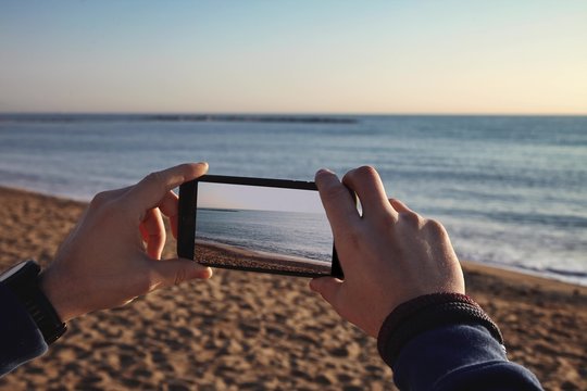 Cinemagraph loop Man hands making video of waves from smart phone on sea shore in sunny winter day, staying on sand beach in jacket