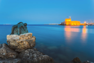 Fototapeta premium Sculpture of an angel on a background of the fortress of St. Nicholas. Rhodes Island. Greece