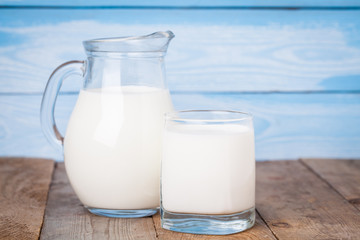 fresh milk in glass jug and glass on wooden table and blue wooden background