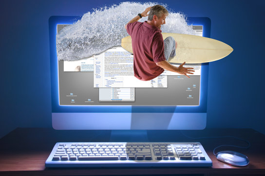 An internet web surfer is literally surfing a wave right through the computer screen with web pages and information on the screen of the computer