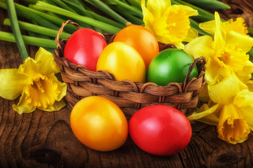 Fototapeta na wymiar Colorful Easter eggs with spring flowers on dark wooden board, sunlight effect