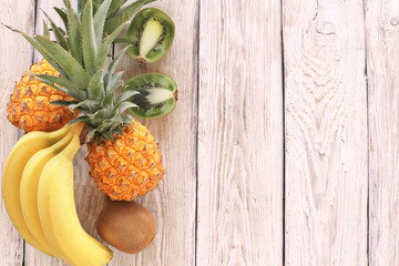 Pineapples, kiwi, bananas on wooden background