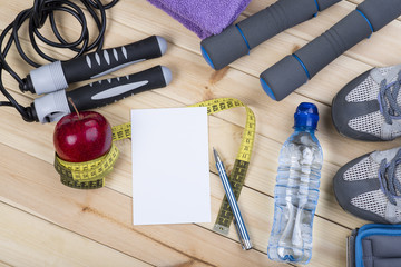 Sport Shoes, Dumbbells, Jump Rope, Towel, Ankle Weights, Tape Measure, Apple, Bottle Of Water, Notepad To Workout Plan On Wooden Floor. Sport Fitness Background
