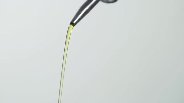 Close up on olive oil being poured from a bottle, white background.