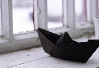 black origami paper ship, boat on old white window