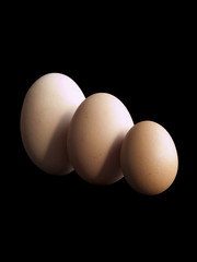 Three eggs of small medium and large size arranged in an overlapping row on a black background. Growth concepts and metaphors.