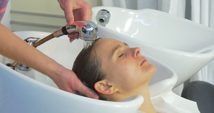 Man Stylist Hairdresser is Washing The Hairs with Bathroom Hose Pipe upon the Sink For a Woman with Long Hairs Face Closed Eyes Beauty Salon