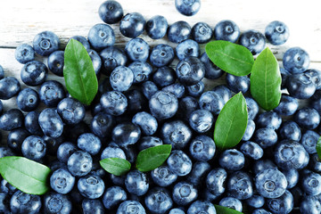 Tasty ripe blueberries with green leaves on wooden table close up