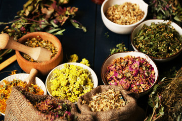 Assortment of dry medicinal herbs in bowls on wooden background top view