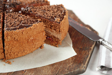 Sliced chocolate cake on wooden table, on light background