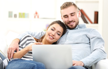 Happy couple sitting on sofa and working on a laptop