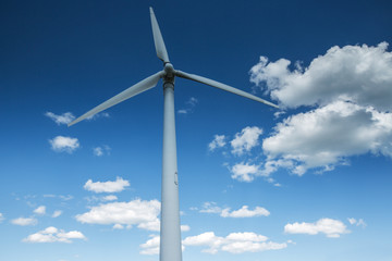 Fototapeta premium Wind energy turbine and fluffy clouds in the sky