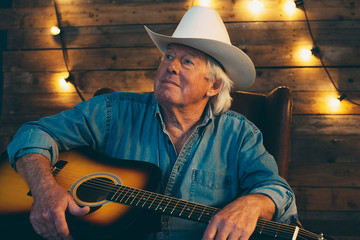 Senior country and western musician sitting with guitar.