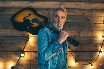 Senior musician with beard holding acoustic guitar on his should