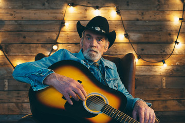 Senior country and western guitarist with beard sitting in chair
