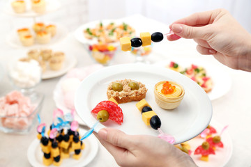 Woman holding plate with snacks and canape on buffet background
