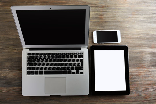 An open silver laptop, mobile phone and modern tablet on the wooden background