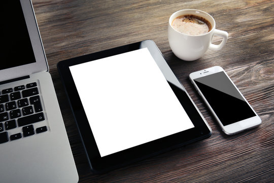 Modern laptop, mobile phone, tablet and coffee cup on wooden table, close-up