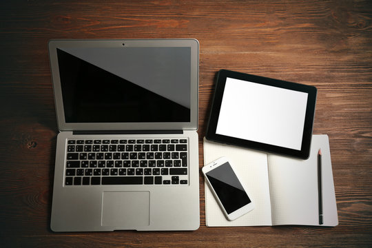 Modern laptop, mobile phone, tablet and notebook on wooden table