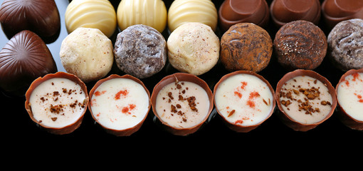 Assorted chocolate candies on black background, close up