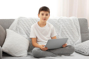 Fototapeta premium Boy with laptop sitting on a sofa at home