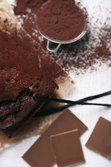 Chocolate cake with cocoa powder, vanilla pods on white table