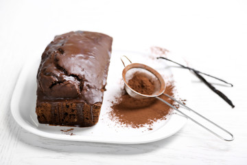 Chocolate cake with icing, cocoa powder and vanilla pods on white table
