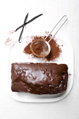 Chocolate cake with icing, cocoa powder and vanilla pods on white table