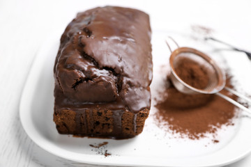 Chocolate cake with icing and cocoa powder on white table