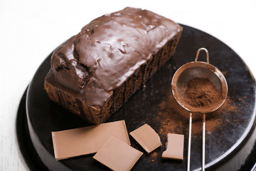 Chocolate cake with icing and cocoa powder on baking dish over white table