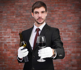 Man holding a bottle of red wine and glass in hands on brick wall background